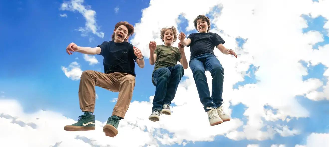 Photo taken from below 3 people jumping in the air with blue sky and clouds overhead.